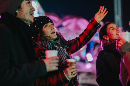 A group of friends gather outdoors during winter, enjoying warm beverages under festive lights.