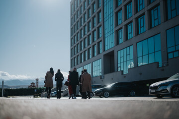 A group of formally dressed individuals walking near a modern building under a bright blue sky. The setting hints at professional, urban, and corporate environments.