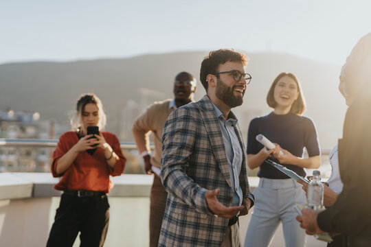 Group of business people enjoying a celebration on a rooftop. They are dancing and socializing, capturing a moment of joy and success against a sunset backdrop.