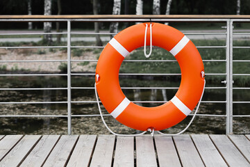 Orange lifebuoy hanging on the fence at the pier near the reservoir.