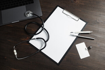 Health care concept. Blank medical clipboard, stethoscope, badge, thermometer, pen and laptop on wooden background.