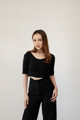 Attractive woman in a black crop top and pants posing against a neutral background