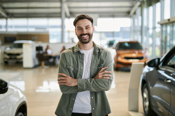 Happy salesperson standing in a car showroom  and looking at camera.