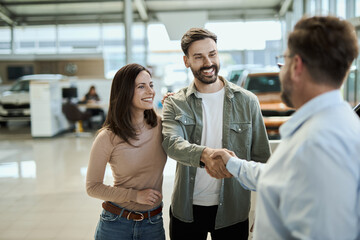 Happy young couple shaking hands with car salesperson in a showroom