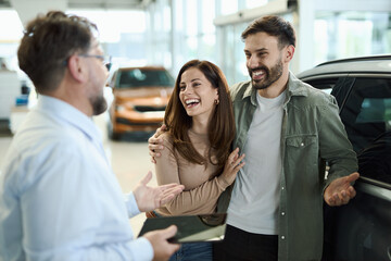 Happy couple talking to car salesperson in a showroom.