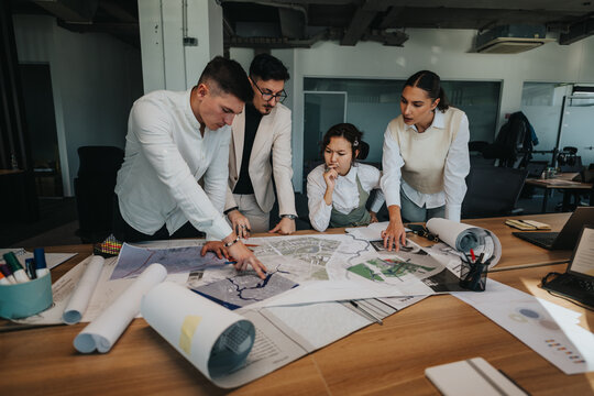 A group of focused business coworkers discusses project plans at a busy office, examining blueprints and maps. The collaborative environment fosters creativity and teamwork in a modern workspace.