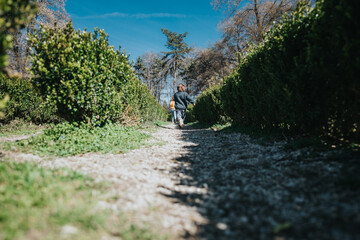 Fototapeta premium A young child strolls along a picturesque garden path framed by lush hedgerows, basking in the pleasant spring weather.