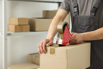 Man using dispenser with adhesive tape to seal cardboard box indoors, closeup. Space for text