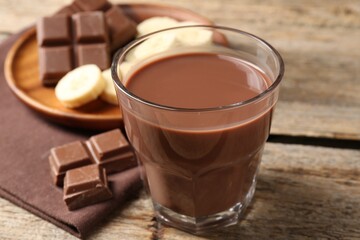 Tasty chocolate milk, pieces and banana on wooden table, closeup