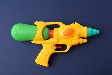 Bright plastic water gun on dark blue background, top view