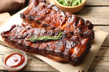 Tasty roasted pork ribs served with rosemary, sauce and salad on wooden table, closeup