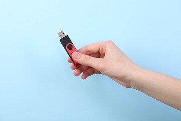 Woman holding USB flash drive on light blue background, closeup