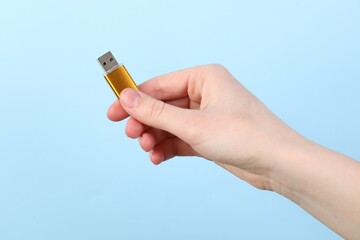 Woman holding USB flash drive on light blue background, closeup