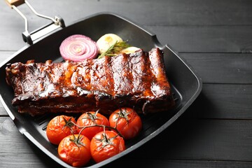 Delicious roasted pork ribs with tomatoes and onions on grey wooden table, closeup