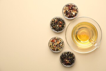 Delicious herbal tea in glass cup and dry leaves on beige background, flat lay. Space for text