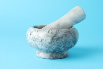 Marble mortar and pestle on light blue background, closeup