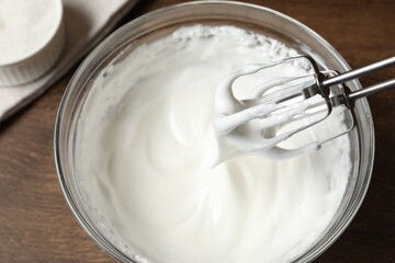 Hand mixer with whisks and bowl of whipped cream on wooden table, above view