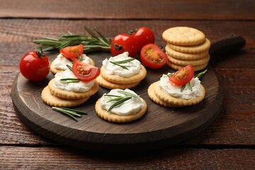 Tasty crackers with cream cheese, rosemary and tomatoes on wooden table, closeup