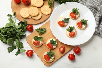 Fototapeta na wymiar Tasty crackers with cream cheese, tomatoes and parsley on white table, flat lay
