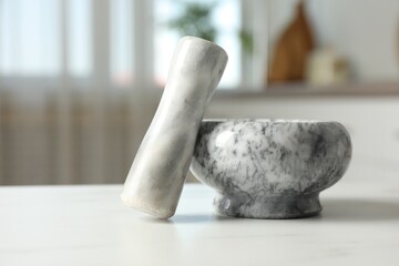 Mortar and pestle on white marble table in kitchen, closeup