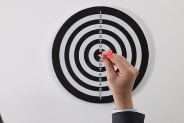 Targeting. Man with arrow aiming at dart board on light background, closeup