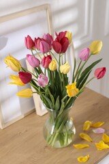 Bouquet of beautiful tulips and frames on wooden table indoors