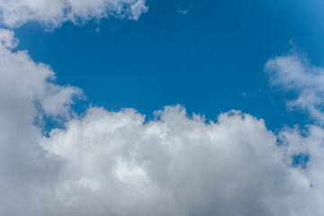 A clear blue sky bordered by soft, white cumulus clouds, creating a peaceful and open atmosphere with ample copy space.