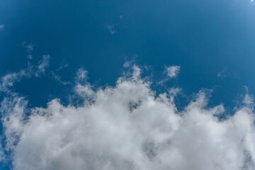 A clear blue sky bordered by soft, white cumulus clouds, creating a peaceful and open atmosphere with ample copy space.