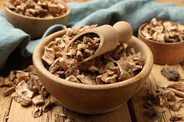 Pieces of dry chicory roots in bowls and scoop on wooden table, closeup