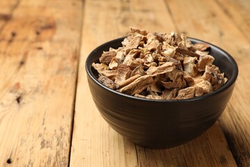 Pieces of dry chicory roots in bowl on wooden table, closeup