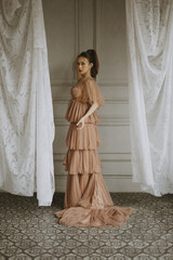 Elegant woman poses in a tiered tulle gown with flowing fabric and lace curtains