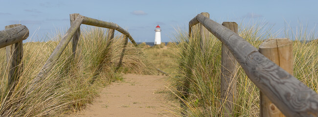 A wooden fence and board walk with a lighthouse in the background