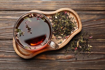 Aromatic herbal tea in glass cup and dry leaves on wooden table, flat lay