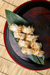 Tuna tataki roll topped with crispy flakes and onions, artfully arranged on a green leaf over a wooden tray.