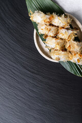 Tuna tataki roll topped with crispy flakes and onions, artfully arranged on a green leaf over a wooden tray.