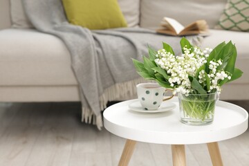 Bouquet of beautiful lily-of-the-valley and cup of tea on coffee table indoors. Space for text