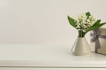 Beautiful lilies of the valley flowers and gift on white table. Space for text