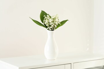 Beautiful lilies of the valley flowers in vase on cabinet