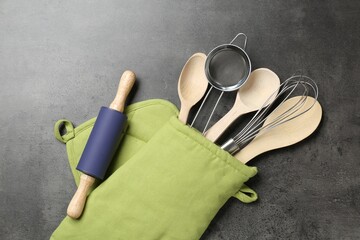 Different kitchen utensils in oven mitten on grey table, flat lay