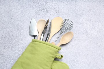 Different kitchen utensils in oven mitten on light table, top view