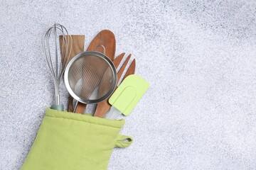 Different kitchen utensils in oven mitten on light table, top view. Space for text