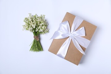 Beautiful lily-of-the-valley flowers and gift on white background, flat lay
