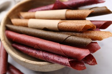 Tasty fruit leather rolls on white marble table, closeup