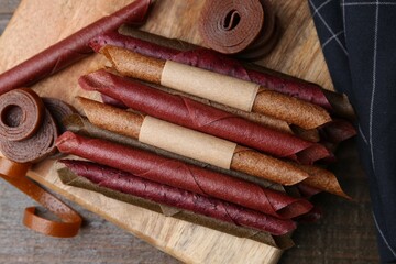 Tasty fruit leather rolls on wooden table, flat lay