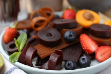 Tasty candied leather rolls, fruits and berries on white table, closeup