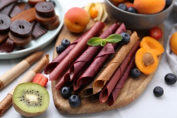 Tasty candied leather rolls, fruits and berries on white table, closeup