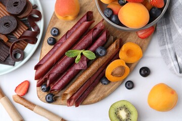 Tasty candied leather rolls, fruits and berries on white table, flat lay