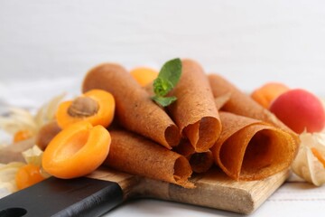 Delicious fruit leather rolls, apricots and physalis on white wooden table, closeup