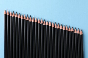 Many sharp graphite pencils on light blue background, flat lay
