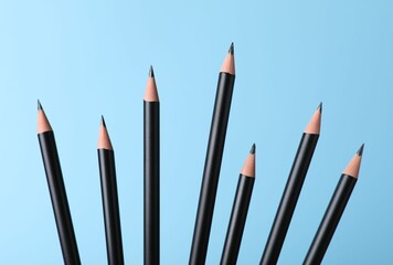 Many sharp graphite pencils on light blue background, closeup